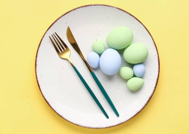 Table setting with Easter eggs and cutlery on yellow background