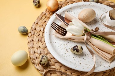 Table serving with Easter eggs and tulip flower on yellow background