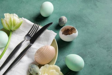 Table serving with Easter eggs and tulip flower on green grunge background, closeup