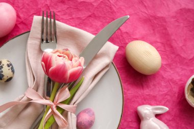 Table serving with Easter eggs and tulip flower on pink background