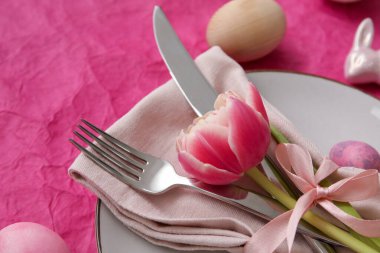 Table serving with Easter eggs and tulip flower on pink background, closeup