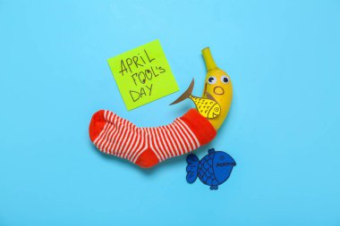 Creative composition with banana, sock and paper decor on color background. April Fool's Day celebration