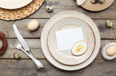 Table setting with blank card, Easter eggs and cutlery on wooden background