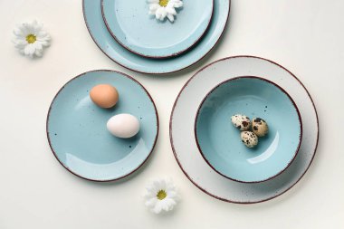 Composition with set of plates, Easter eggs and chrysanthemum flowers on white background