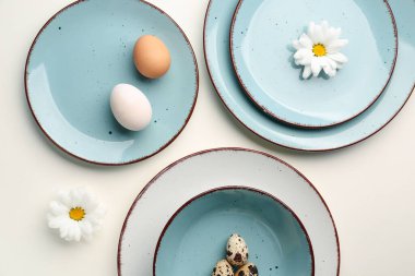 Composition with set of plates, Easter eggs and chrysanthemum flowers on white background