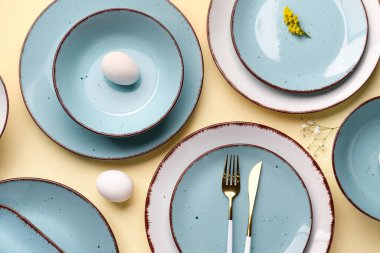 Composition with set of plates, cutlery, Easter eggs and floral decor on beige background