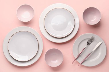 Set of plates and bowls with cutlery on pink background