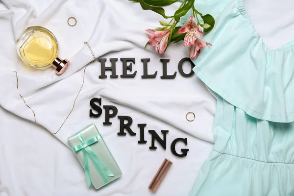Composition with text HELLO SPRING, cosmetics, accessories, gift box and dress on light fabric background