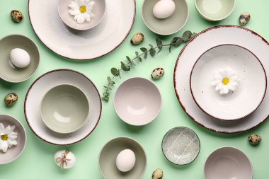 Composition with crockery, Easter eggs and chrysanthemum flowers on green background