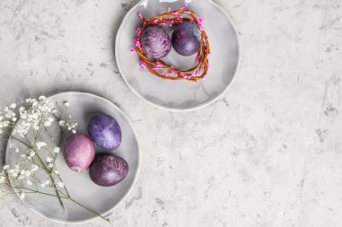 Plates with painted Easter eggs and gypsophila flowers on light background