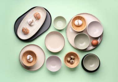 Set of plates and bowls with Easter eggs on green background