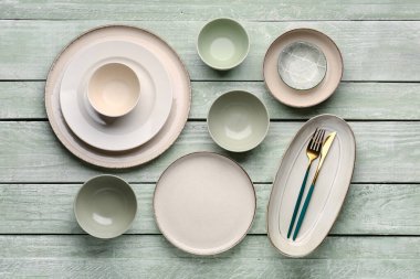 Set of plates and bowls with cutlery on green wooden background