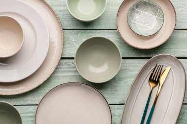 Set of plates and bowls with cutlery on green wooden background