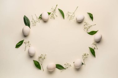 Frame made of Easter eggs, green leaves and gypsophila flowers on white background