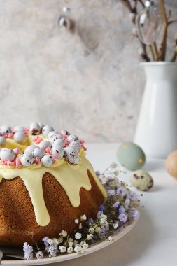 Plate with tasty Easter cake, eggs and gypsophila flowers on light table, closeup