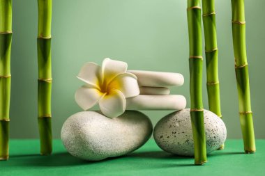Stack of spa stones, flower and bamboo on green background