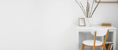 Table with willow branches in vase and chair near white wall in room. Banner for design