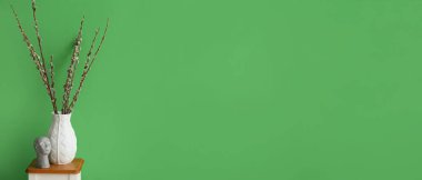 Vase with willow branches and decor on table near green wall. Banner for design