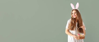 Beautiful young woman with Easter basket and bunny ears on color background with space for text