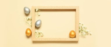 Beautiful Easter composition with blank frame, painted eggs and flowers on beige background