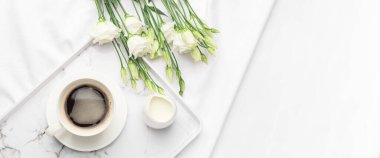Tray with cup of coffee, jug of milk and flowers on bed. Banner for design