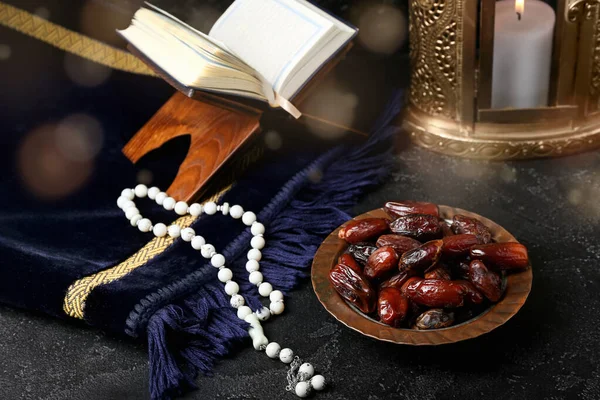 Plate with dates and prayer beads, Quran book and fanous lamp on dark background