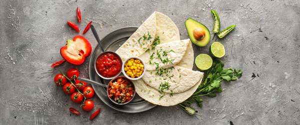 Bowls of tasty salsa sauces with tortilla on grunge background, top view