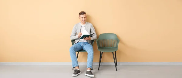 Young man reading book near beige wall. Banner for design