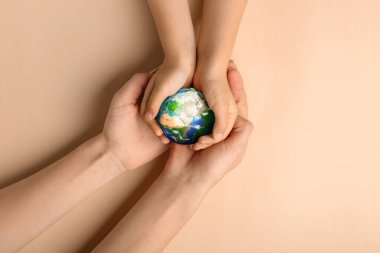 Hands of mother and child holding small planet Earth on beige background