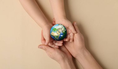 Hands of mother and child holding small planet Earth on beige background