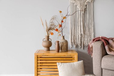 Vases with tree branches, flowers and pampas grass on table near light wall