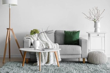 Interior of living room with sofa, flowers and tree branches in vases