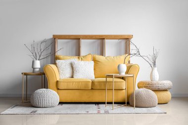 Interior of living room with yellow sofa and tree branches in vases