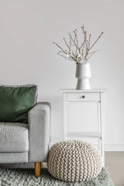 Vase with tree branches and flowers on table in light living room