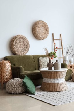 Interior of living room with green sofa, rattan poufs and vases