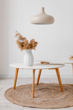 Vase with pampas grass on table near light wall in room