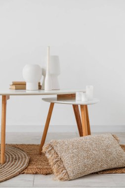 Vases with candles and books on tables in light room
