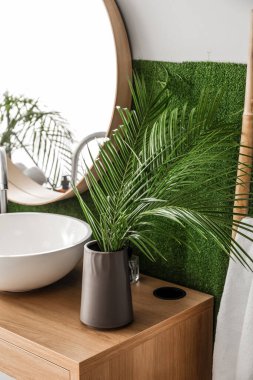 Vase with palm leaves and sink on table in bathroom