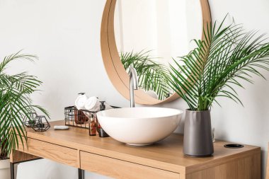 Vase with palm leaves, sink and cosmetic products on table in bathroom