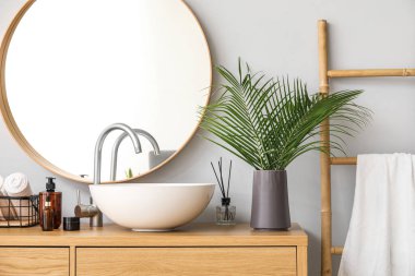 Vase with palm leaves, sink and cosmetic products on table in bathroom