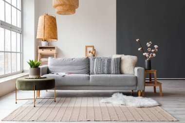 Cozy interior of living room with grey sofa, pouf and fur carpet near window