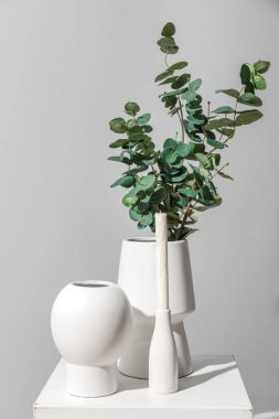 Vases with eucalyptus branches and candle on table near grey wall