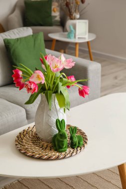 Vase with tulips and Easter rabbits on table in living room