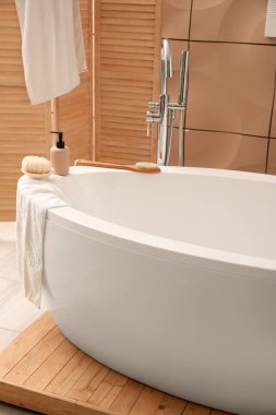 Interior of bathroom with modern bathtub, folding screen and towels