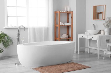 Interior of light bathroom with bathtub, table and sink