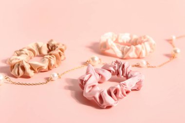 Silk scrunchies and necklace on pink background, closeup