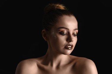 Young woman with golden glitter makeup on black background, closeup