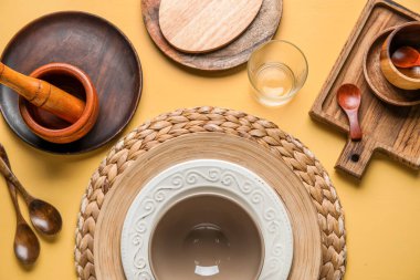 Beautiful table setting with plates, bowl and spoons on yellow background