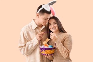 Happy young couple in bunny ears with Easter eggs and rabbit on beige background