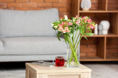 Vase with alstroemeria flowers, cup of tea and magazine on table in living room